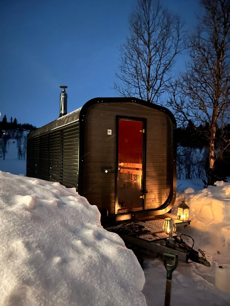 Fjellbadstue omgitt av snø med varm belysning, klar for badstuopplevelse i fjellet.